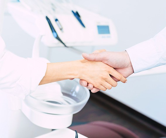 Dentist and patient shaking hands in front of treatment chair