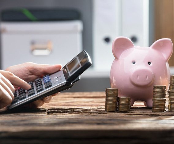 Hands operate pocket calculator next to piggy bank